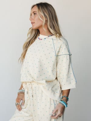A cream and soft blue polka dot matching set — relaxed sweatshirt top with contrast stitching and drawstring pants — styled with layered beaded bracelets and a colorful beaded necklace for that effortlessly put-together, cozy-day energy.