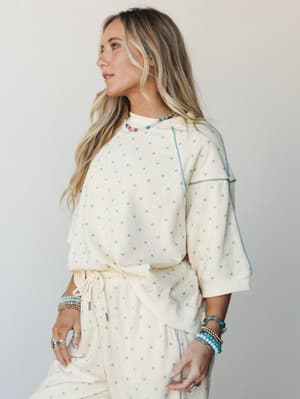 A cream and soft blue polka dot matching set — relaxed sweatshirt top with contrast stitching and drawstring pants — styled with layered beaded bracelets and a colorful beaded necklace for that effortlessly put-together, cozy-day energy.