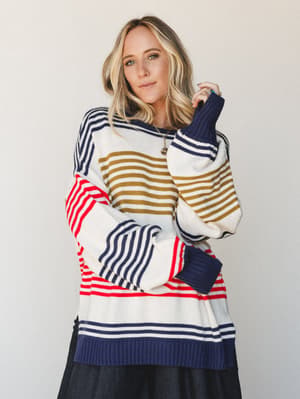 A relaxed, oversized mixed-stripe sweater in cream, navy, red, and olive layered over a black wide-leg pant — the kind of effortless combo that looks like you tried just enough.