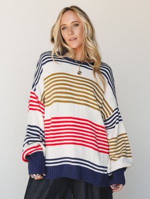An oversized striped knit sweater in cream, navy, red, and olive worn with wide-leg black pants — relaxed, lived-in, and the kind of top you'd reach for on a crisp weekend without thinking twice.