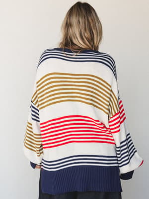 Shot from behind, a model wears an oversized multicolor striped knit sweater with a relaxed, boxy silhouette — the kind of cozy, expressive piece that does all the talking for you.