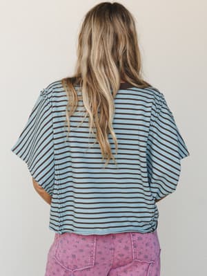 A back-view shot of a relaxed striped tee in dusty blue and brown, styled with floral pink pants — effortless and a little unexpected in the best way.