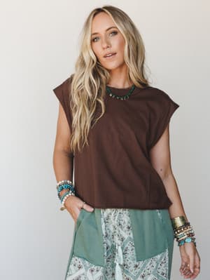 A relaxed cropped muscle tee in deep chocolate brown styled with patchwork boho pants and layers of beaded bracelets — the kind of effortless combo that looks intentional without trying.