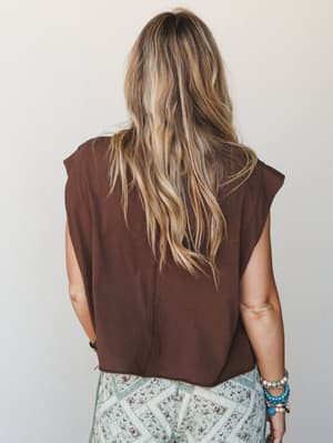 A back-view shot of a relaxed cropped tee in deep chocolate brown, paired with a printed sage-and-brown patterned bottom and stacked turquoise bracelets — effortless and earthy with just enough personality.