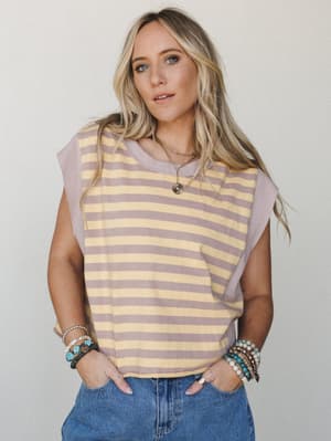 A relaxed striped muscle tee in soft yellow and dusty lavender styled with denim and stacked boho bracelets — the kind of effortless top that looks like you tried just the right amount.