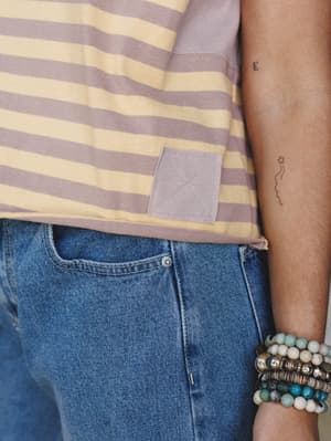 A close-up shot of a striped tee tucked loosely into medium-wash denim, styled with a stack of beaded bracelets — the kind of effortless, personal detail that makes a simple outfit feel completely yours.