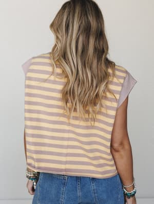 Back view of a striped crop tee in warm mustard and dusty mauve, paired with denim and stacked boho bracelets — the kind of top that looks like you didn't try too hard but absolutely did.