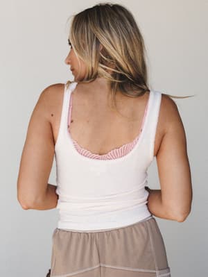 Back view of a fitted ribbed tank with a scoop back neckline, a pink lace bra peeking out underneath, paired with taupe casual shorts — soft, lived-in, and effortlessly comfortable.
