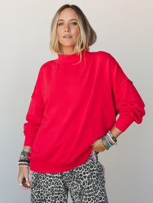 An oversized red mock-neck sweatshirt styled with leopard print pants and stacked beaded bracelets — the kind of effortless, personality-forward outfit that looks like it came together in five minutes but somehow feels completely intentional.