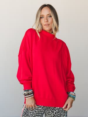 A bold red oversized mock-neck sweatshirt styled with stacked beaded bracelets and a peek of leopard-print pants — effortlessly expressive and lived-in, like your favorite Saturday top that also works for wherever the day takes you.
