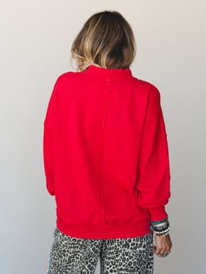 A back-view shot of a bold red pullover sweatshirt with a center back seam detail, styled with leopard print pants and a stack of beaded bracelets — casual and confident with just enough personality.