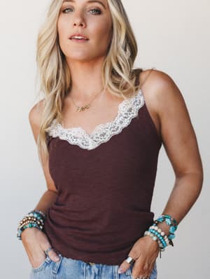 A wine-toned ribbed cami with delicate white lace trim at the neckline, styled with stacked turquoise bracelets and a gold 'mama' necklace — casual but personal, like her everyday uniform with a little extra.