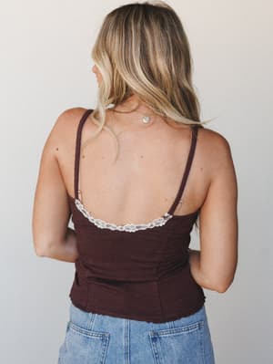 A back-view shot of a deep brown cami with delicate lace trim along the low back neckline, paired with light wash denim — relaxed, a little romantic, and very wearable.
