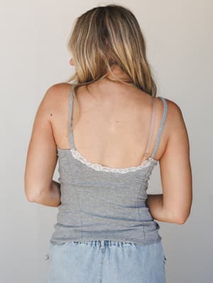 A back-facing shot of a heather grey ribbed cami with a delicate lace trim neckline, paired with light wash denim — effortless and soft, like something you'd reach for without thinking twice.