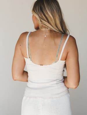 Shot from behind, this soft oatmeal lace-trim cami layers over a white textured skirt — the back necklace detail and velvet straps doing quiet, pretty work against a neutral studio backdrop.