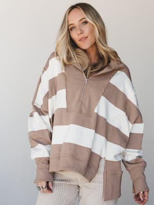 An oversized quarter-zip pullover in warm mocha and cream wide stripes, styled with ribbed wide-leg pants and stacked silver rings — the kind of effortless, cozy outfit you wear when you want to look like you tried without actually trying.