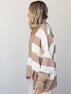 A side-profile shot of a model in an oversized quarter-zip pullover with bold wide stripes in mocha and cream — the kind of cozy, relaxed layer that works just as hard on a coffee run as it does on the couch.