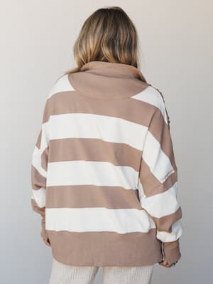 A back-view shot of an oversized striped pullover in warm mocha and cream, styled with wide-leg ribbed pants — the kind of sweater you reach for every single Saturday without thinking twice.