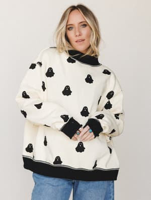 An oversized cream sweatshirt covered in an all-over black ghost print, styled with wide-leg blue jeans and stacked silver and turquoise rings — cozy, playful, and just the right amount of spooky.