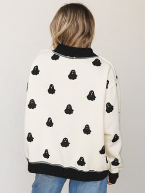 A back-view shot of an oversized cream sweatshirt covered in an allover black ghost print, styled with light wash jeans — the kind of piece that makes Halloween feel like a whole personality, not just a holiday.