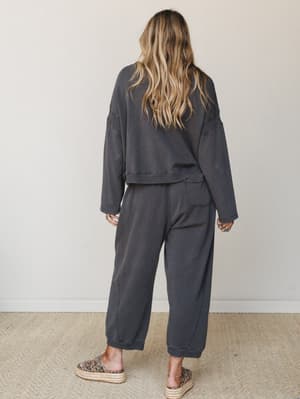 Shot from behind, a model wears a matching washed charcoal sweat set — cropped pullover and relaxed joggers — styled with leopard print platform espadrilles and stacked rings for that effortless, lived-in feel.