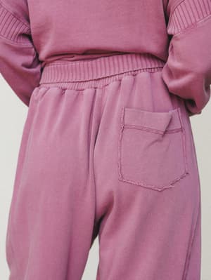 A close-up back view of mauve fleece sweatpants with a raw-edge patch pocket and ribbed elastic waistband, styled as a matching set with a coordinating crewneck sweatshirt.