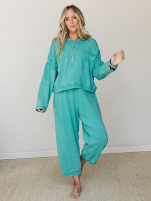 A matching turquoise sweat set — cropped pullover and wide-leg joggers — styled with layered gold necklaces and beaded bracelets for that effortless 'ran errands, looked great' energy.