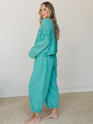 A matching washed teal sweat set — oversized pullover and relaxed joggers — styled barefoot against a soft neutral wall, giving off that effortlessly cozy, staying-in-but-make-it-cute energy.