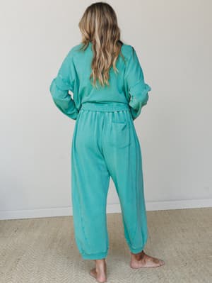 Shot from the back, a model in a matching washed teal sweat set — oversized pullover and relaxed joggers — has that effortless 'just threw this on and it's somehow perfect' energy against a clean studio backdrop.