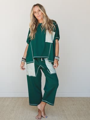 A breezy two-piece matching set in deep forest green with contrast color-block panels and visible contrast stitching — worn barefoot and stacked in bracelets, it reads effortlessly relaxed without trying too hard.
