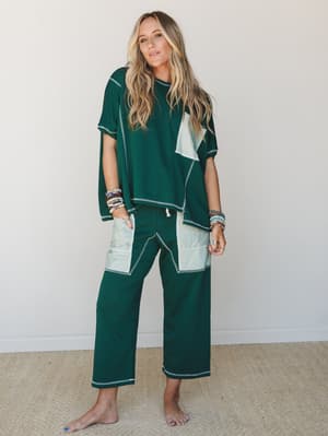 A relaxed two-piece matching set in deep forest green with contrast mint color-block panels and visible contrast stitching throughout — styled with stacked beaded bracelets and bare feet for an effortlessly cozy, lived-in feel.