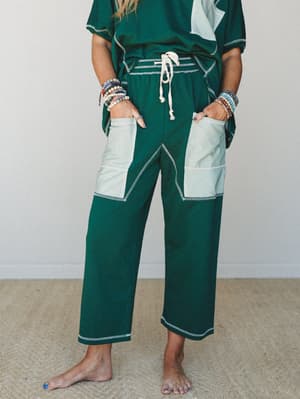 A cropped mid-shot of a matching green set styled casually — wide-leg pants with contrast stripe patch pockets and a drawstring waist steal the focus, layered with stacks of beaded bracelets that give the whole look a relaxed, collected feel.