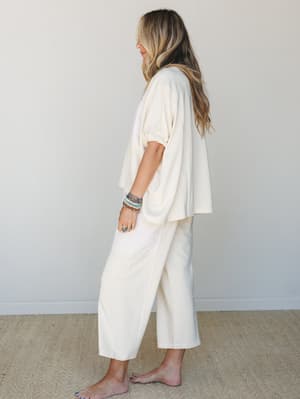 A side-profile shot of a cream-toned matching set — oversized short-sleeve top and wide-leg cropped pants — styled with stacked boho bracelets and silver rings, giving off that effortlessly relaxed, 'didn't try too hard but looks great' energy.