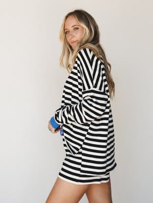 A relaxed striped short set shot against a clean studio wall — the bold black and white stripes hit different with that cobalt blue cuff detail peeking through, giving the whole look an easy, confident energy.