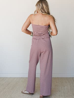 Shot from the back, a matching striped two-piece set in dusty mauve and dark burgundy — strapless tube top and wide-leg pants — styled with layered bracelets and sandals for an easy, warm-weather feel.