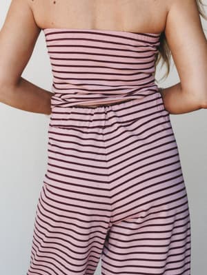 A close back-view shot of a matching striped two-piece set — a strapless tube top and wide-leg pants — in a soft mauve pink with burgundy stripes, styled together with a peek of midriff between the pieces.