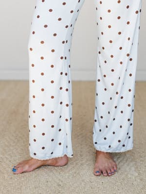 A close-up of wide-leg lounge pants in cream with warm brown polka dots, finished with a delicate lace hem trim — the kind of pants you wear all morning and then just... don't change out of.