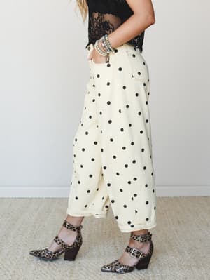 A side-profile shot of wide-leg cream polka dot pants paired with a black lace crop top, leopard print block heels, and stacked beaded bracelets — playful and a little unexpected in the best way.
