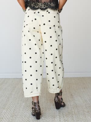 A back-view shot of wide-leg, barrel-fit cropped pants in cream with bold black polka dots, styled with a black lace top and leopard print heeled booties — the kind of outfit that has a personality before you even say hello.