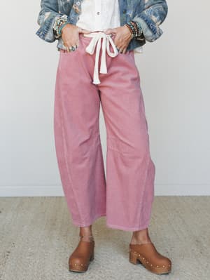 Wide-leg corduroy barrel pants in a soft mauve pink, styled with an embroidered denim jacket, white tie-front blouse, and studded wood clogs — the kind of laid-back outfit that looks completely intentional.