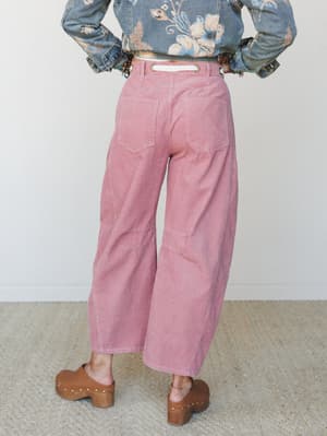 Shot from behind, a model shows off wide-leg barrel corduroy pants in a soft mauve paired with a floral denim jacket and wood-heeled clogs — the kind of outfit that makes a Saturday feel intentional.