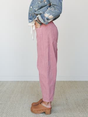 A side-profile shot of dusty pink corduroy barrel-leg pants styled with a floral-embroidered denim jacket, layered bracelets, and wooden clogs — relaxed and expressive with a vintage-boho nod.