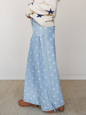 A side-profile shot of a polka dot denim maxi skirt styled with a cream star-print sweater and tan studded clogs — the kind of outfit that feels nostalgic and intentional at the same time.