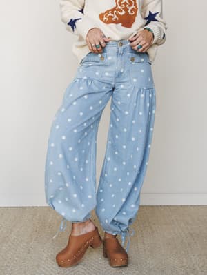 A mid-shot of wide-leg polka dot denim pants styled with a cream intarsia knit sweater and tan studded clogs — playful and personality-forward, with silver rings and a turquoise bracelet adding that collected, effortless boho finish.