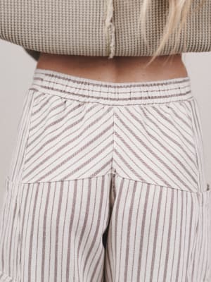Close-up of a person wearing a beige textured top and striped pants.