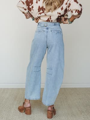 Shot from behind, this look pairs light-wash barrel jeans — complete with a back buckle detail and subtle distressing — with a cow print sweater and chunky wood-heel clogs, landing somewhere between Western-casual and effortlessly cool.