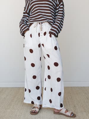 Wide-leg linen-look pants in off white with oversized terracotta polka dots, styled with a brown and white striped crochet sweater and buckle sandals — the kind of outfit that looks intentional without trying.