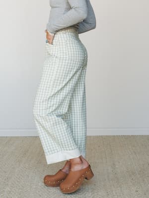 A side-profile shot of sage green gingham barrel-leg pants styled with a grey long-sleeve top and brown leather clogs — relaxed and a little vintage, like something you'd reach for on a good Saturday.