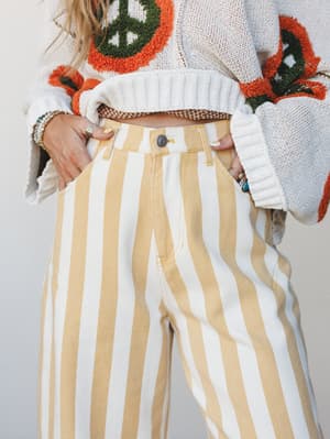 A close-up mid-shot of wide-leg striped pants in warm butter yellow and cream, styled with a cropped peace-sign crochet sweater and layered rings and bracelets — the kind of outfit that looks effortless but was absolutely thought about.