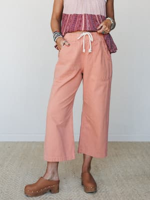 Wide-leg cropped pants in a warm dusty coral styled with a printed boho top, stacked bracelets, and wooden clogs — the kind of effortless daytime outfit that looks like it came together without trying.